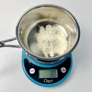 Flour is added to the saucepan sitting on top of the scale.