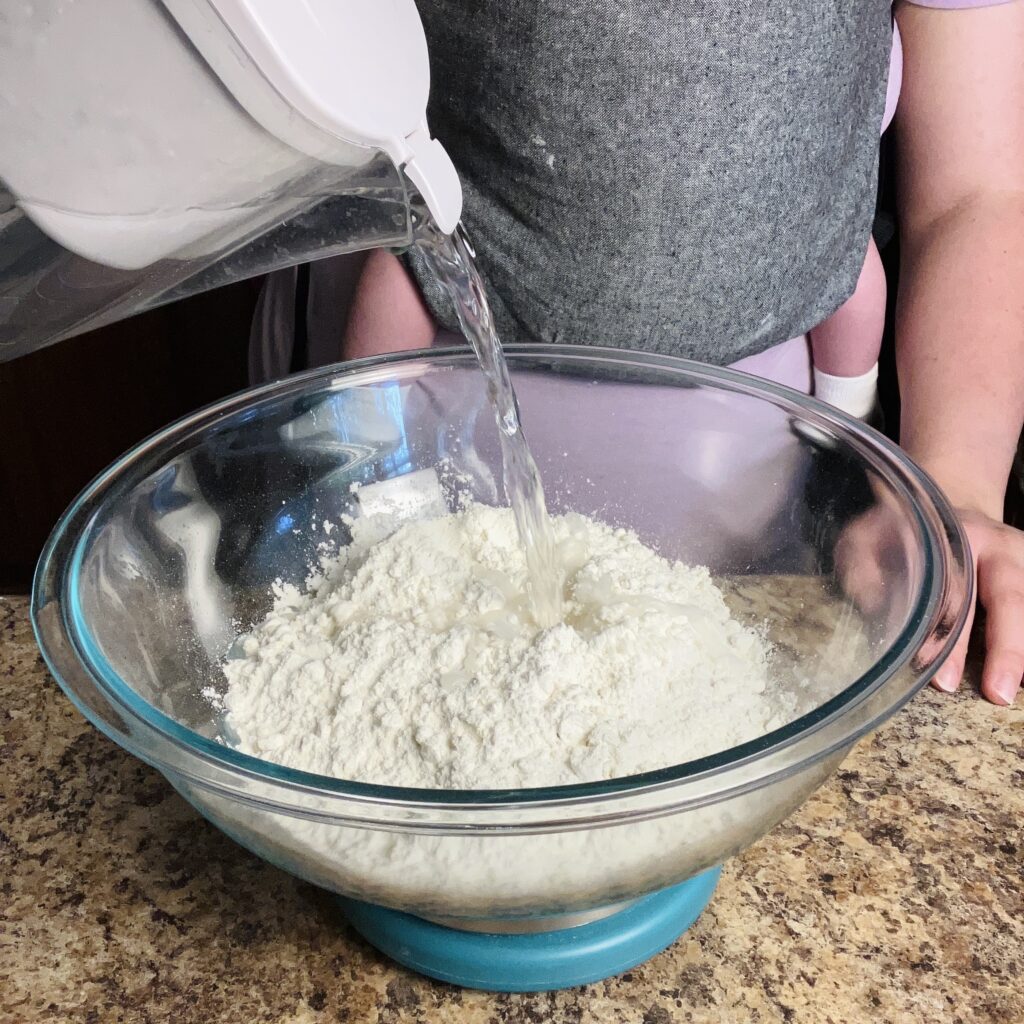 pouring water into flour to make bread dough